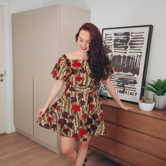 Brown, red, white, and black African Oti floral textured leaf pattern on Knee length high-low dreads off the shoulder skater dress with slightly flared quarter sleeves, featuring Pockets on each side.
