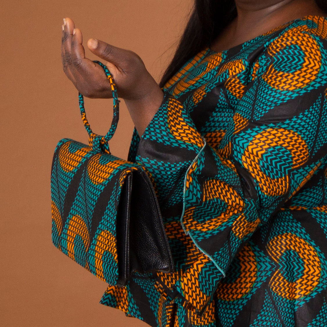 Leather bag with ring shaped handle, velvet lined interior and a geometic orange and green African Print overlay