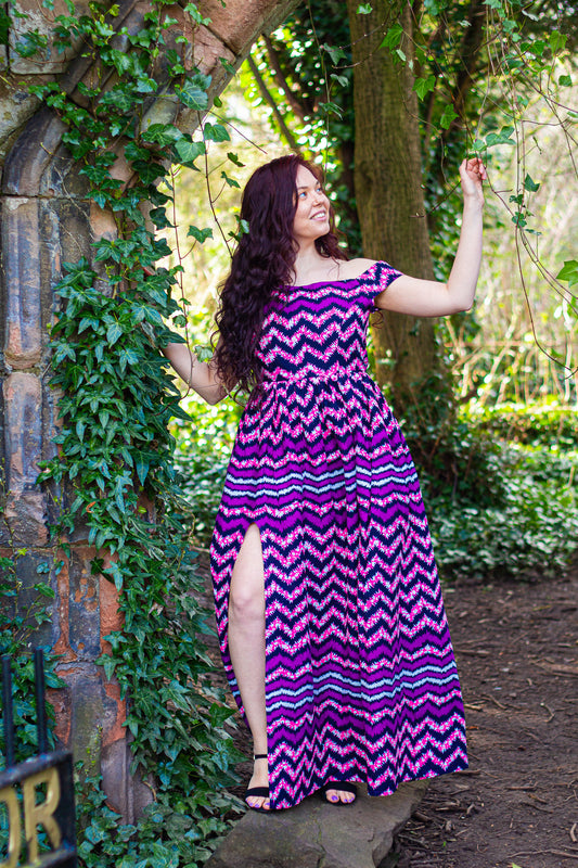 Purple and black African zig-zag texture over-laying a lilac, blue and whites spotted-mesh Ankara wax print on a floor length, short off the shoulder sleeved skater skirt, maxi dress with a thigh high slit.
