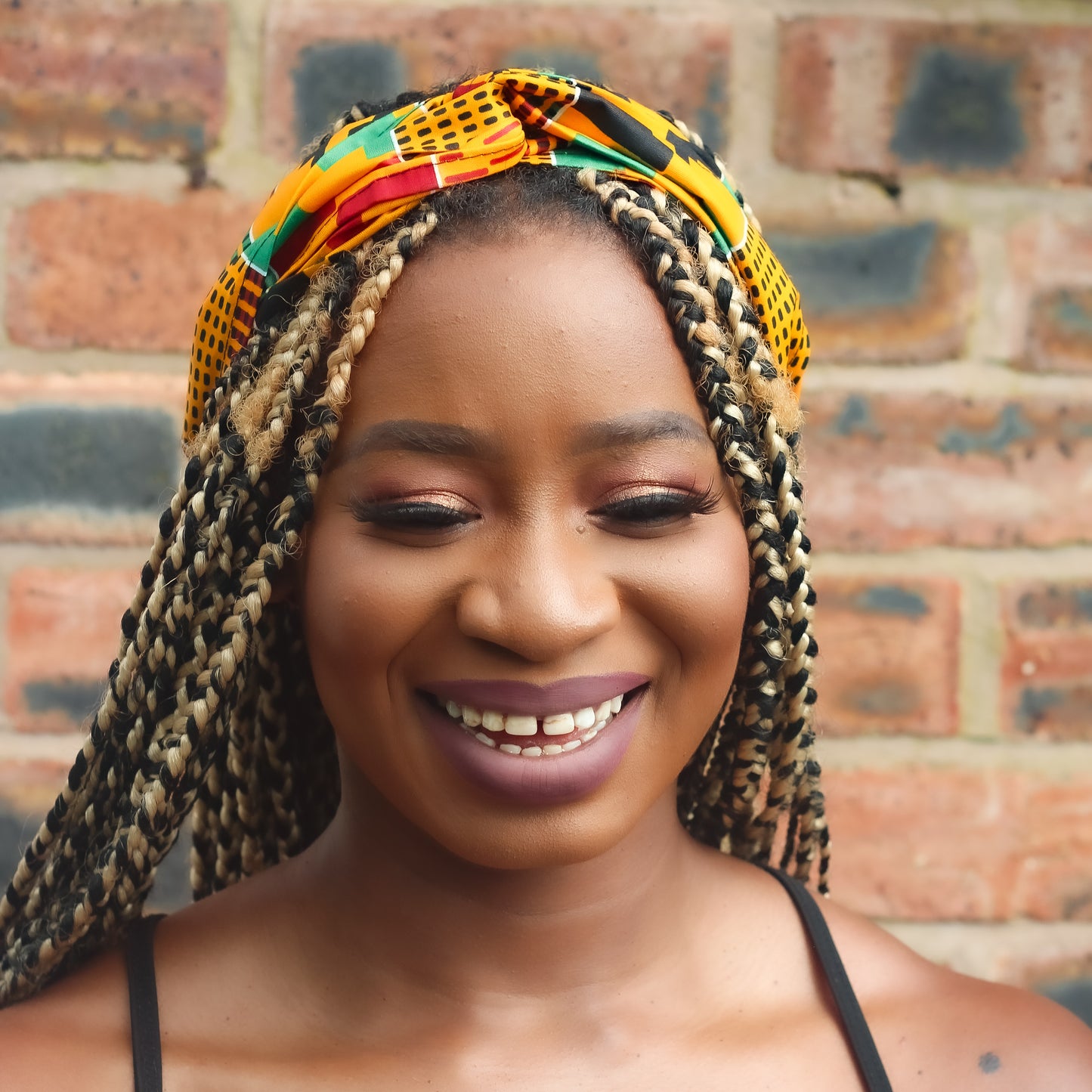 Yellow, green, red, and black African print head wrap tied as headband in a geo-shaped pattern, made from sustainably sourced Ankara wax print.
