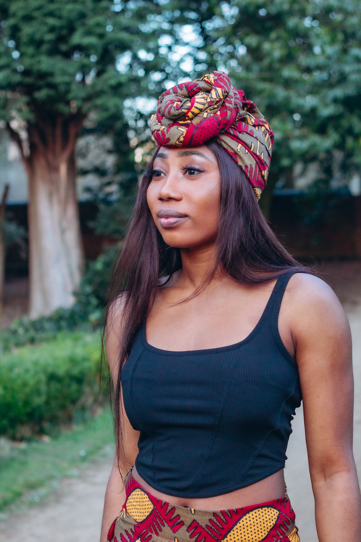 Red, yellow and brown African print head wrap tied a turban in graphic floral pattern, made from sustainably sourced Ankara wax print.