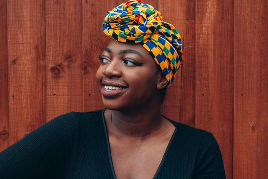 Yellow, green, blue, red and black African print head wrap tied as turban in a checkered pattern, made from sustainably sourced Ankara wax print.