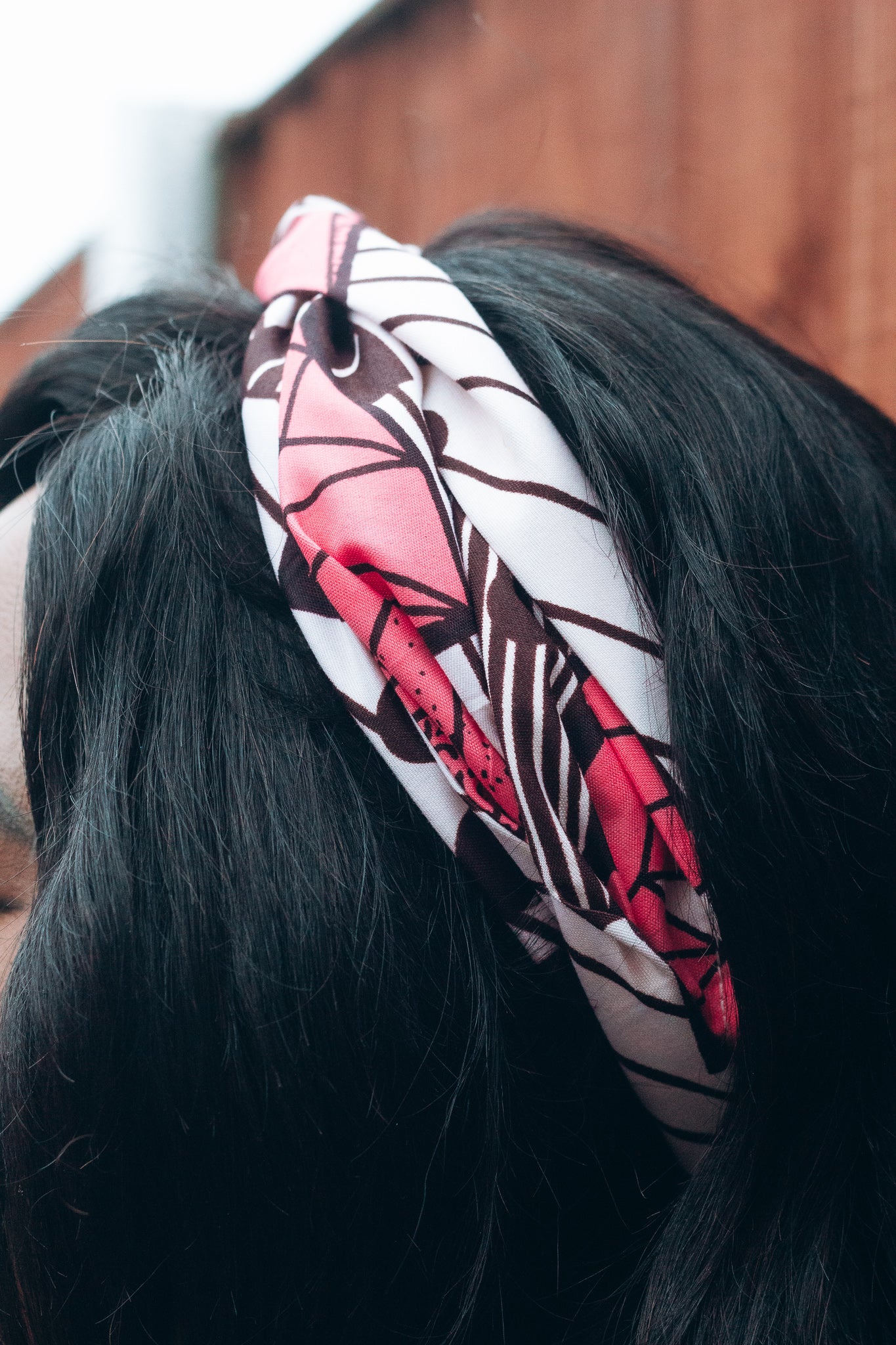 Red, white, and brown African print head wrap tied as headband in a geo- Flora pattern, made from sustainably sourced Ankara wax print.
