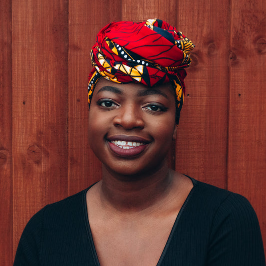 red, yellow, white, and black African print head wrap tied as a turban in a graphic pattern, made from sustainably sourced Ankara wax print.