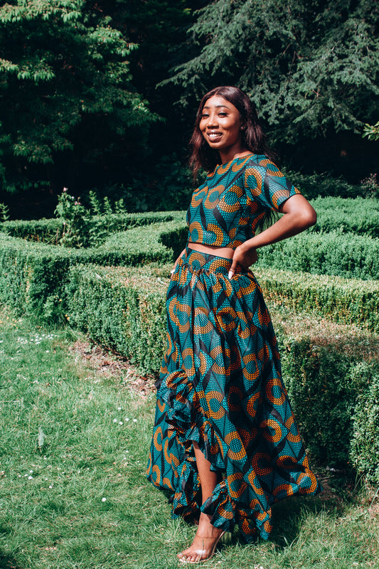 Orange, green and black African printed floor length high to low maxi skirt with a thigh high slit with ruffle detailed and seamed belt in a circle geo-shaped pattern, made from sustainably sourced Ankara wax print.