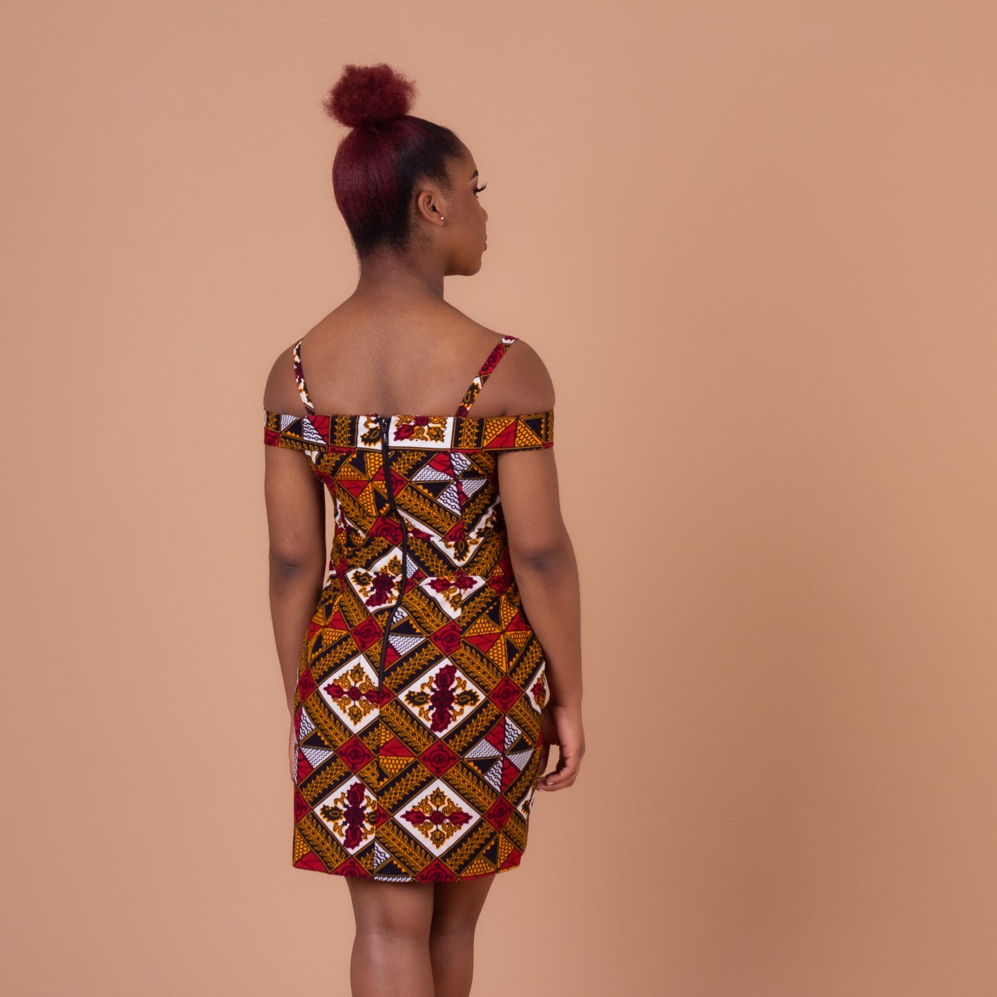 Red, yellow, white, and black Ankara wax print In African floral medallion pattern on a above knee high open pleated panelled dress with sweetheart neckline dress with off the shoulder straps, detailed with smaller spaghetti straps.