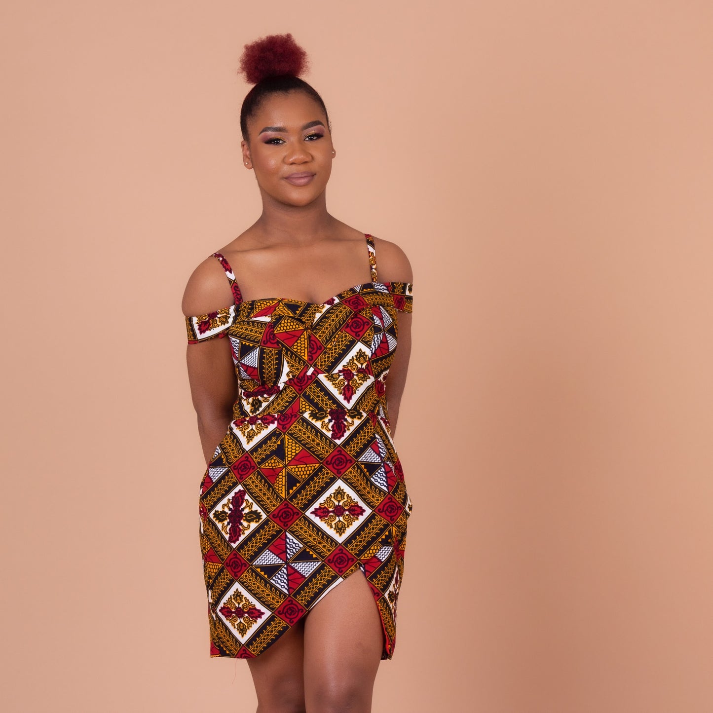 Red, yellow, white, and black Ankara wax print In African floral medallion pattern on a above knee high open pleated panelled dress with sweetheart neckline dress with off the shoulder straps, detailed with smaller spaghetti straps.