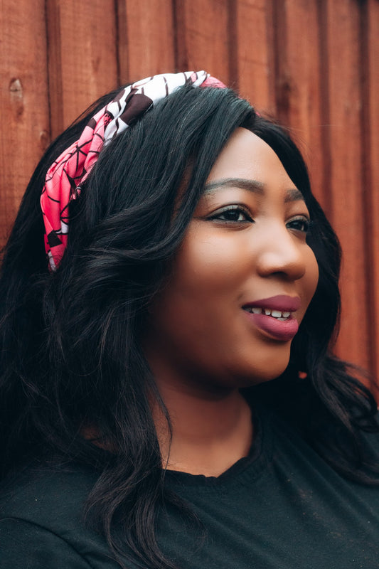 Red, white, and brown African print head wrap tied as headband in a geo- Flora pattern, made from sustainably sourced Ankara wax print.
