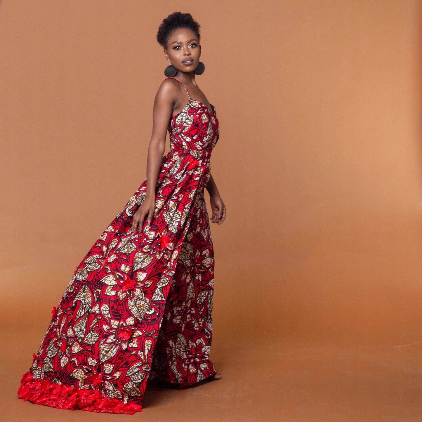 Ankara wax print in the bold African floral red, cream and light brown Ade fabric floor-length gown featuring a sweetheart neckline, closed back and off-shoulder straps with a matching outer cape belt.