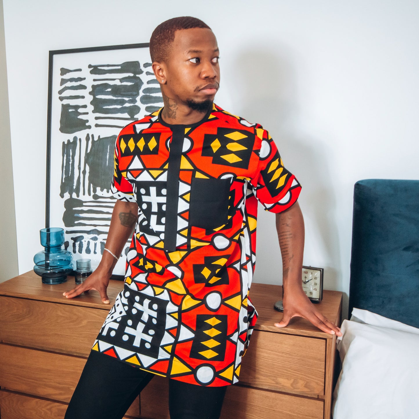 Black man in short sleeved African print kaftan in red, black, white and yellow pattern