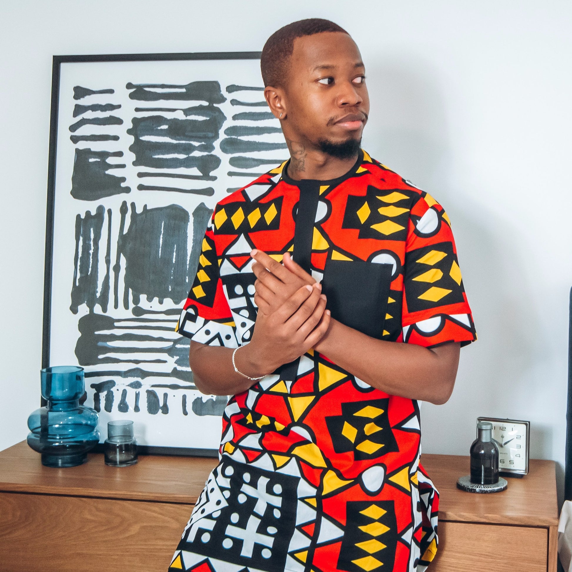 Black man in short sleeved African print kaftan in red, black, white and yellow pattern
