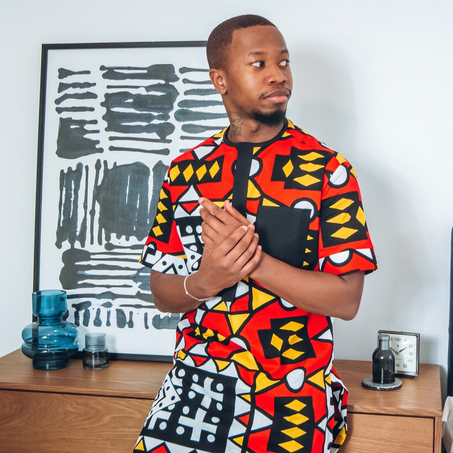 Black man in short sleeved African print kaftan in red, black, white and yellow pattern
