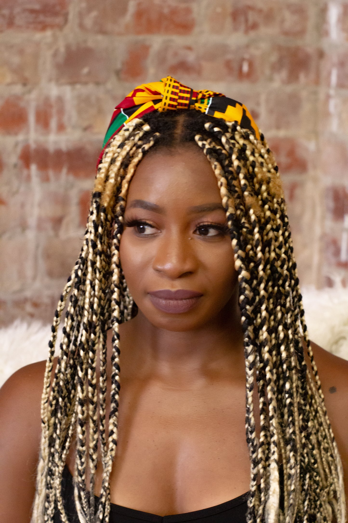 ellow, green, red, and black African print head wrap tied as headband in a geo-shaped pattern, made from sustainably sourced Ankara wax print.