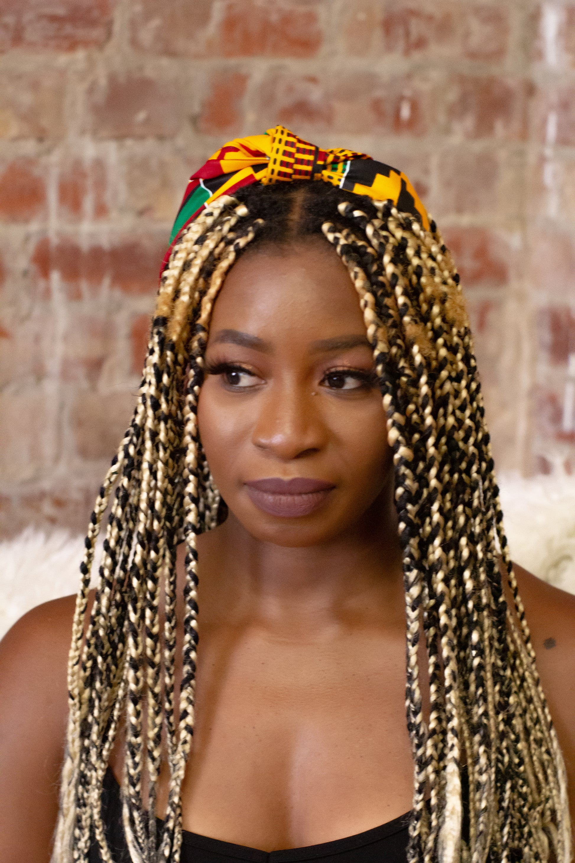ellow, green, red, and black African print head wrap tied as headband in a geo-shaped pattern, made from sustainably sourced Ankara wax print.