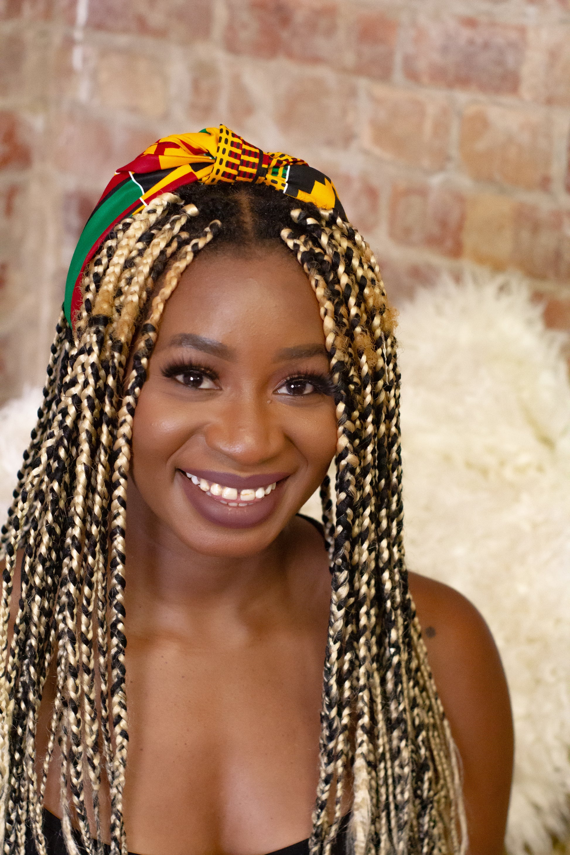ellow, green, red, and black African print head wrap tied as headband in a geo-shaped pattern, made from sustainably sourced Ankara wax print.