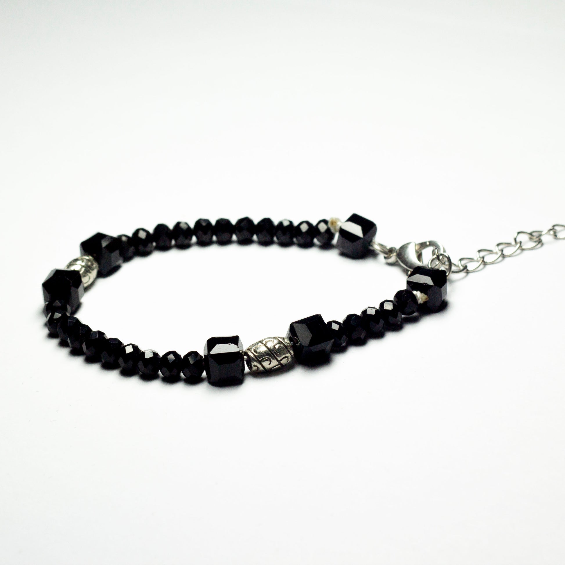 Black beaded bracelet made of black crystal beads featuring engraved cylinder pendants and a chain clasp design