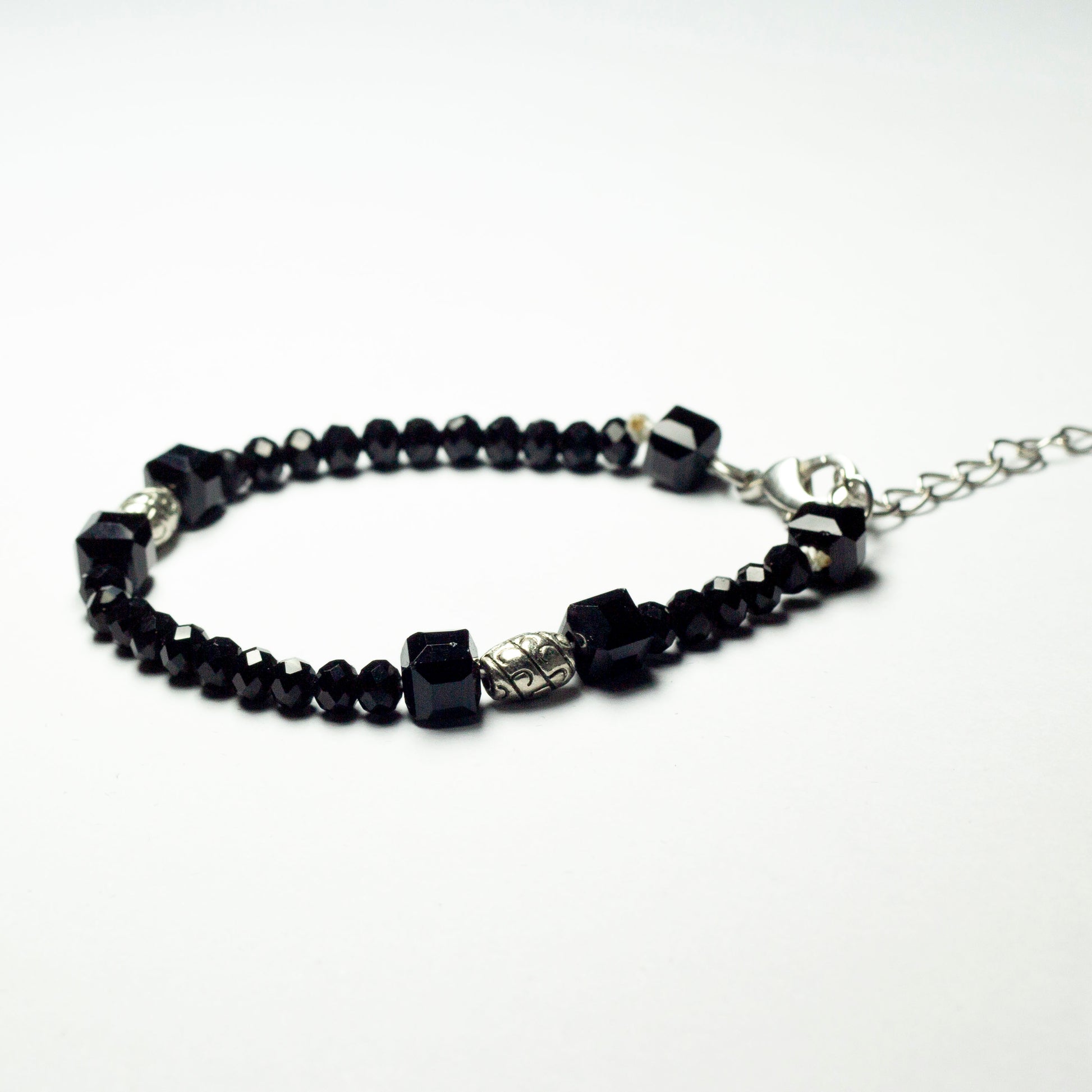 Black beaded bracelet made of black crystal beads featuring engraved cylinder pendants and a chain clasp design
