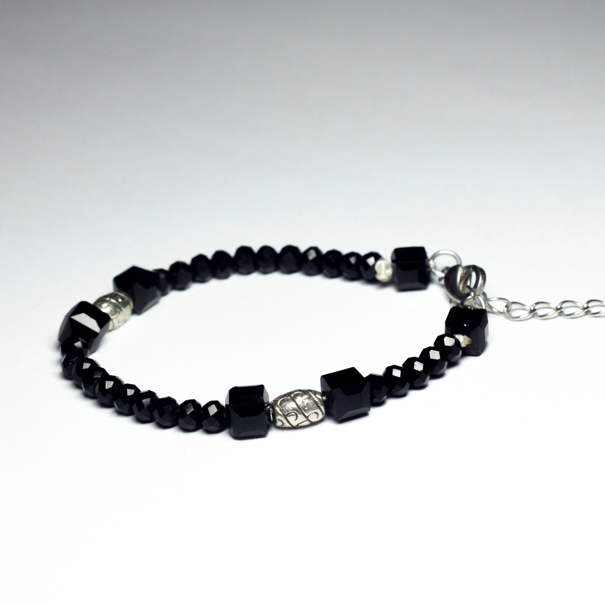 Black beaded bracelet made of black crystal beads featuring engraved cylinder pendants and a chain clasp design