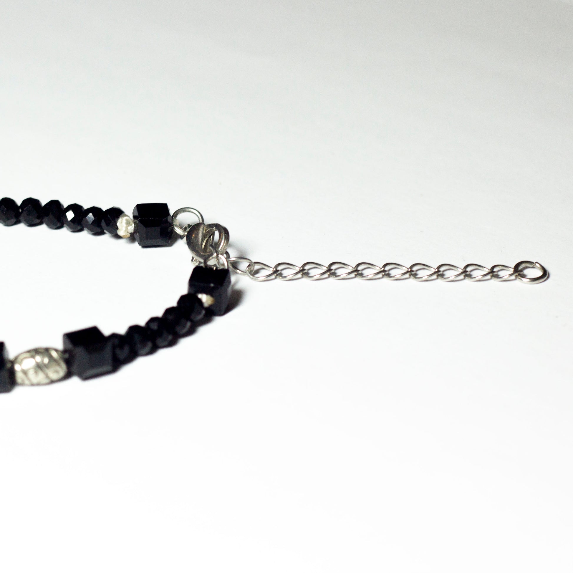 Black beaded bracelet made of black crystal beads featuring engraved cylinder pendants and a chain clasp design