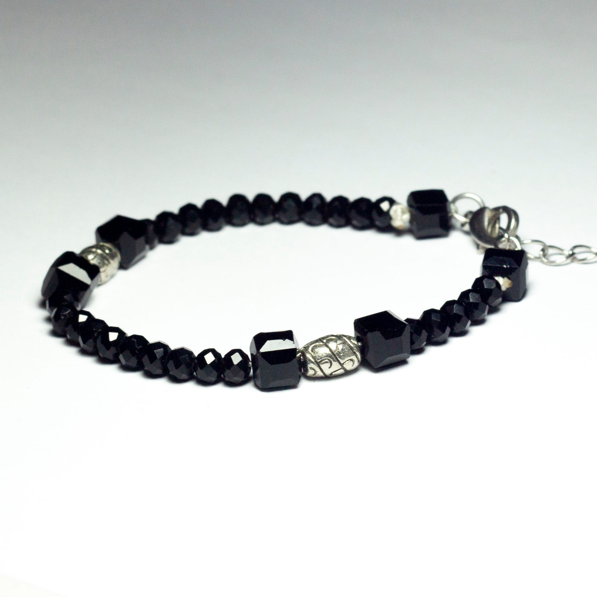 Black beaded bracelet made of black crystal beads featuring engraved cylinder pendants and a chain clasp design