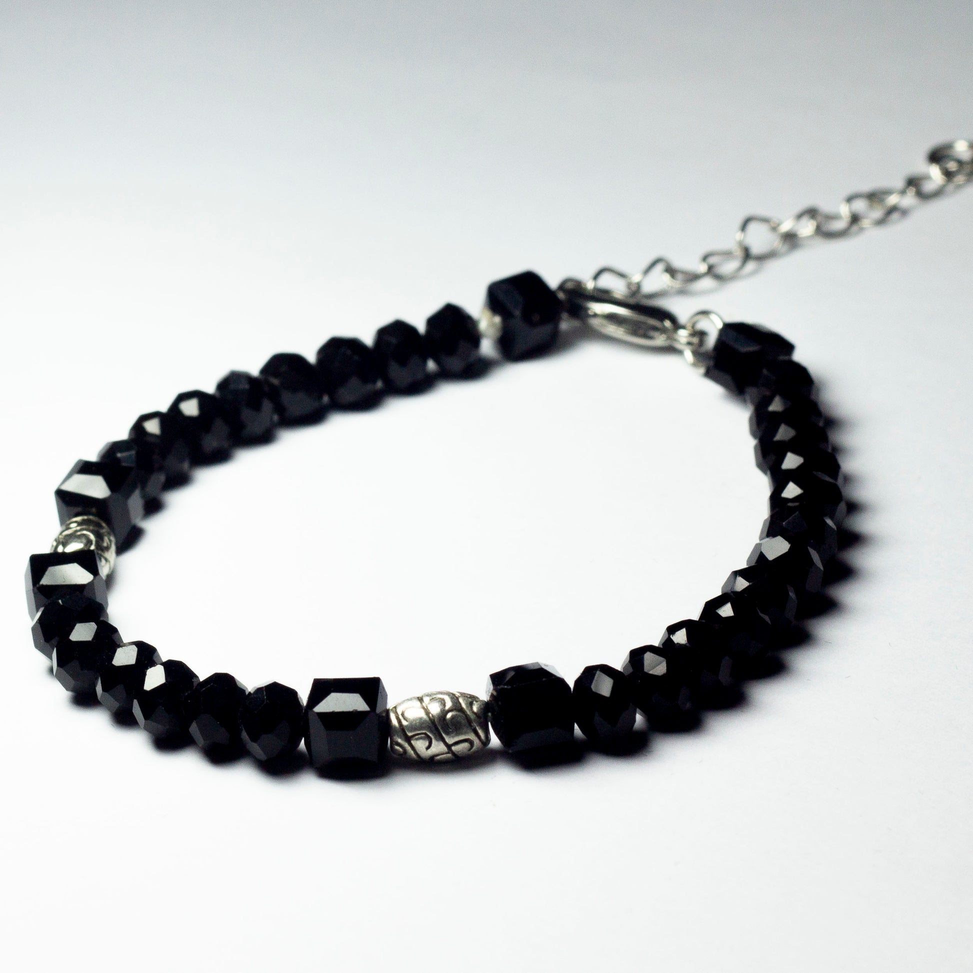 Black beaded bracelet made of black crystal beads featuring engraved cylinder pendants and a chain clasp design
