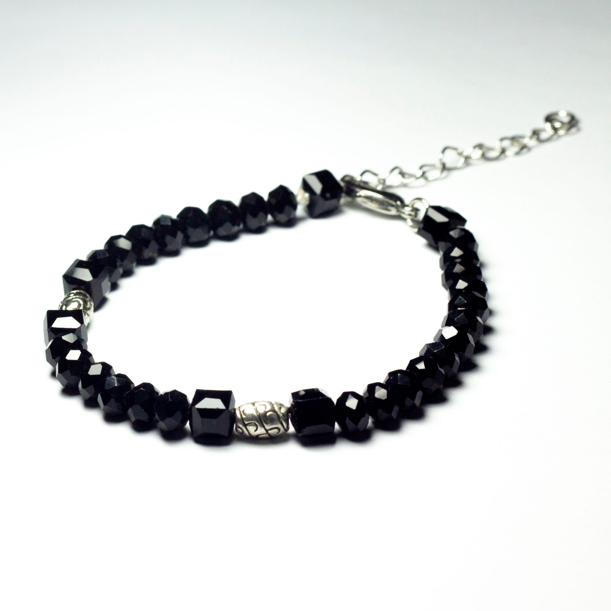 Black beaded bracelet made of black crystal beads featuring engraved cylinder pendants and a chain clasp design