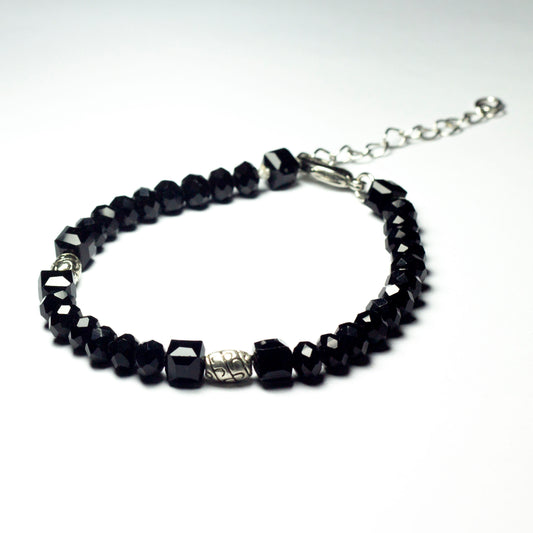 Black beaded bracelet made of black crystal beads featuring engraved cylinder pendants and a chain clasp design