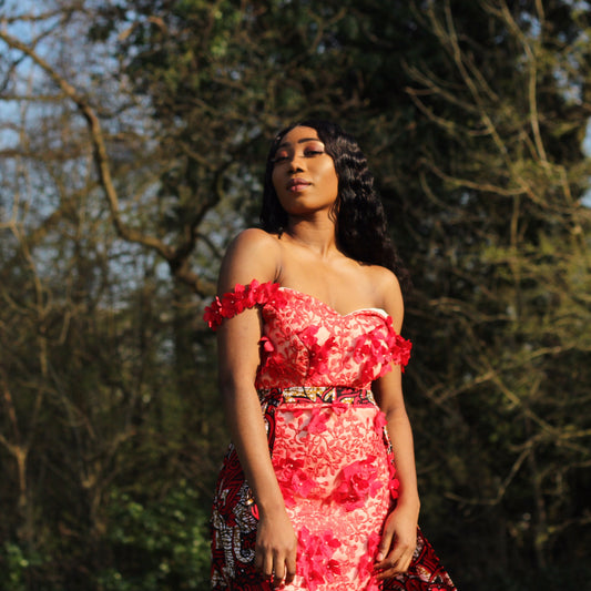 A floral red Ankara wax print fabric floor length gown with sweetheart neckline, off the shoulder floral straps, red inner lace,  an outer cape belt with appliqué red flowers featuring embellished lace detailing. 