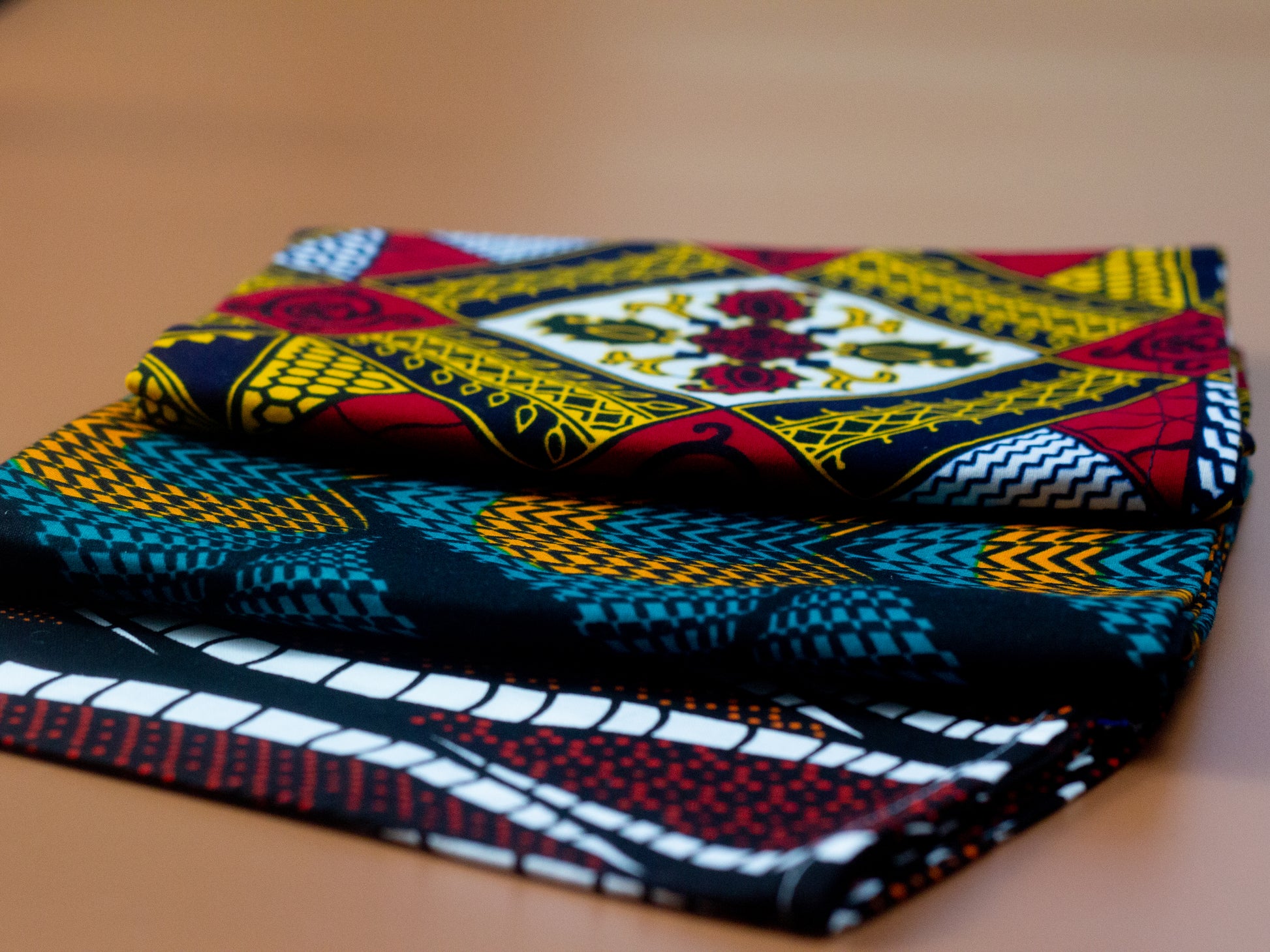 Orange, green and black African print head wrap fabric in a circle geo-shaped pattern, made from sustainably sourced Ankara wax print. Brown, red, white, and black African print head wrap fabric in a floral pattern, made from sustainably sourced Ankara wax print Brown, red, white, and black African print head wrap fabric in a floral pattern, made from sustainably sourced Ankara wax print..