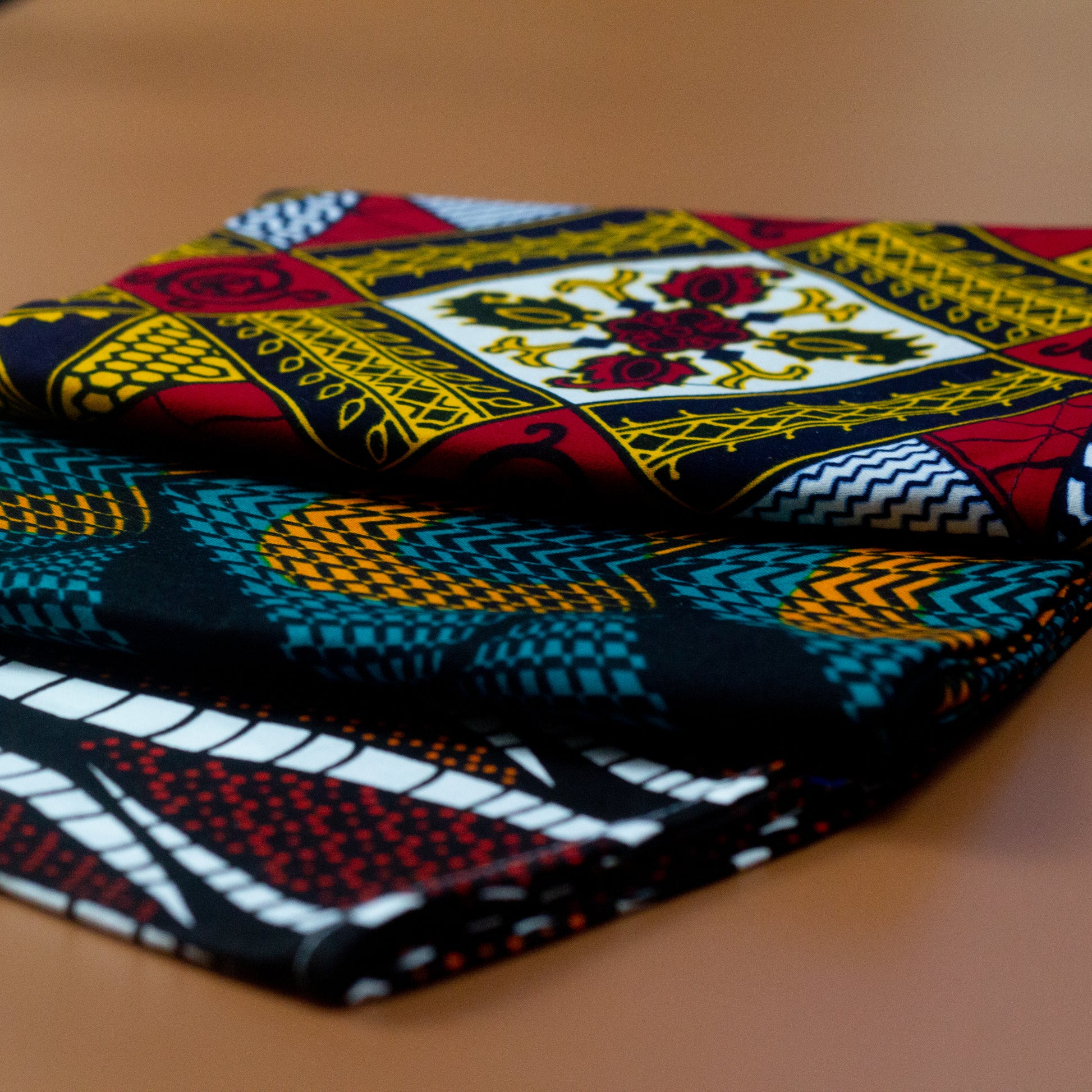 Orange, green and black African print head wrap fabric in a circle geo-shaped pattern, made from sustainably sourced Ankara wax print. Brown, red, white, and black African print head wrap fabric in a floral pattern, made from sustainably sourced Ankara wax print Brown, red, white, and black African print head wrap fabric in a floral pattern, made from sustainably sourced Ankara wax print..