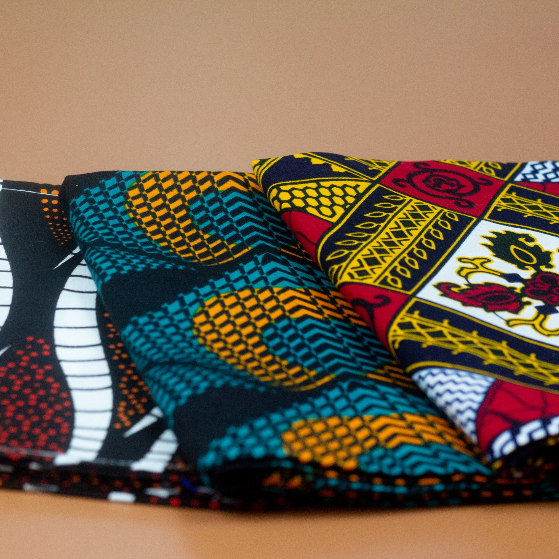 Orange, green and black African print head wrap fabric in a circle geo-shaped pattern, made from sustainably sourced Ankara wax print. Brown, red, white, and black African print head wrap fabric in a floral pattern, made from sustainably sourced Ankara wax print Brown, red, white, and black African print head wrap fabric in a floral pattern, made from sustainably sourced Ankara wax print..