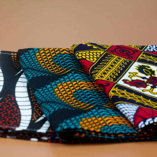 Orange, green and black African print head wrap fabric in a circle geo-shaped pattern, made from sustainably sourced Ankara wax print. Brown, red, white, and black African print head wrap fabric in a floral pattern, made from sustainably sourced Ankara wax print Brown, red, white, and black African print head wrap fabric in a floral pattern, made from sustainably sourced Ankara wax print..