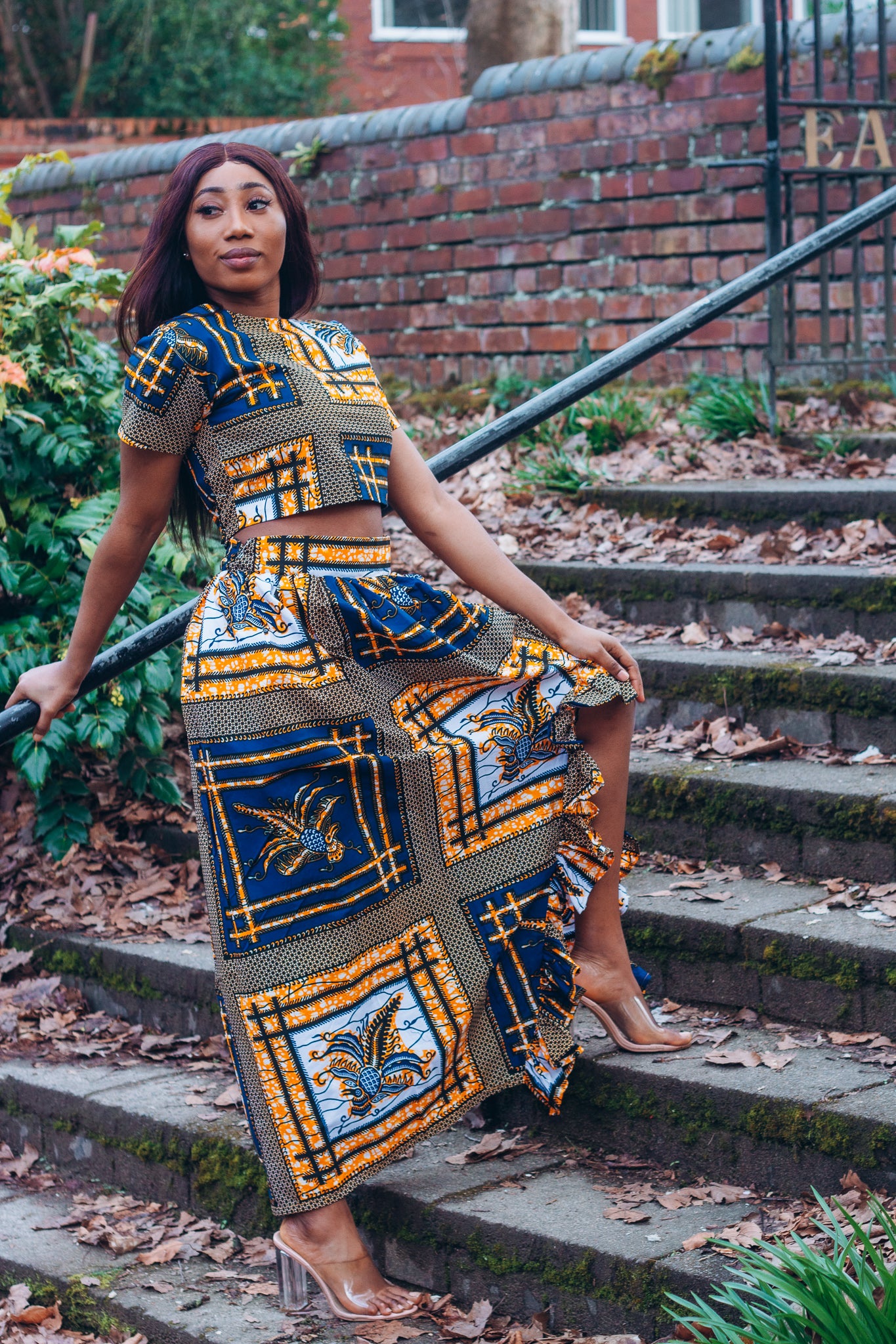 yellow, white, and black Ankara wax print In African floral medallion pattern floor length high to low maxi skirt with a thigh high slit with ruffle detailed and seamed belt made from sustainably sourced Ankara wax print.