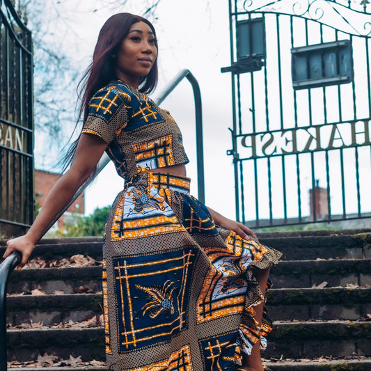 yellow, white, and black Ankara wax print In African floral medallion pattern floor length high to low maxi skirt with a thigh high slit with ruffle detailed and seamed belt made from sustainably sourced Ankara wax print.