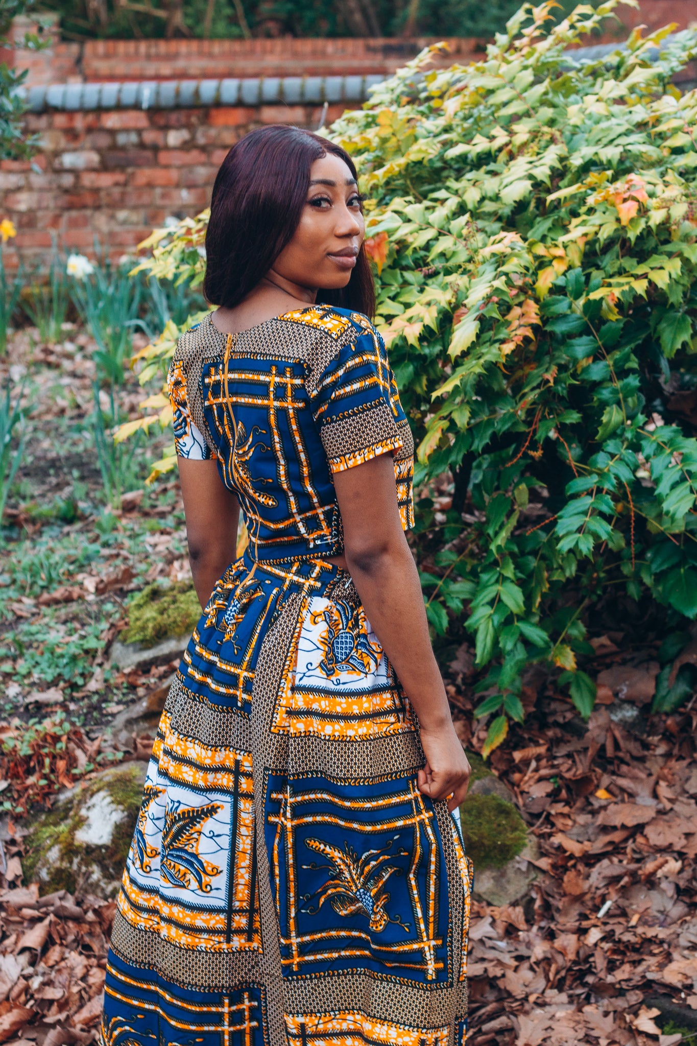 yellow, white, and black Ankara wax print In African floral medallion pattern floor length high to low maxi skirt with a thigh high slit with ruffle detailed and seamed belt made from sustainably sourced Ankara wax print.