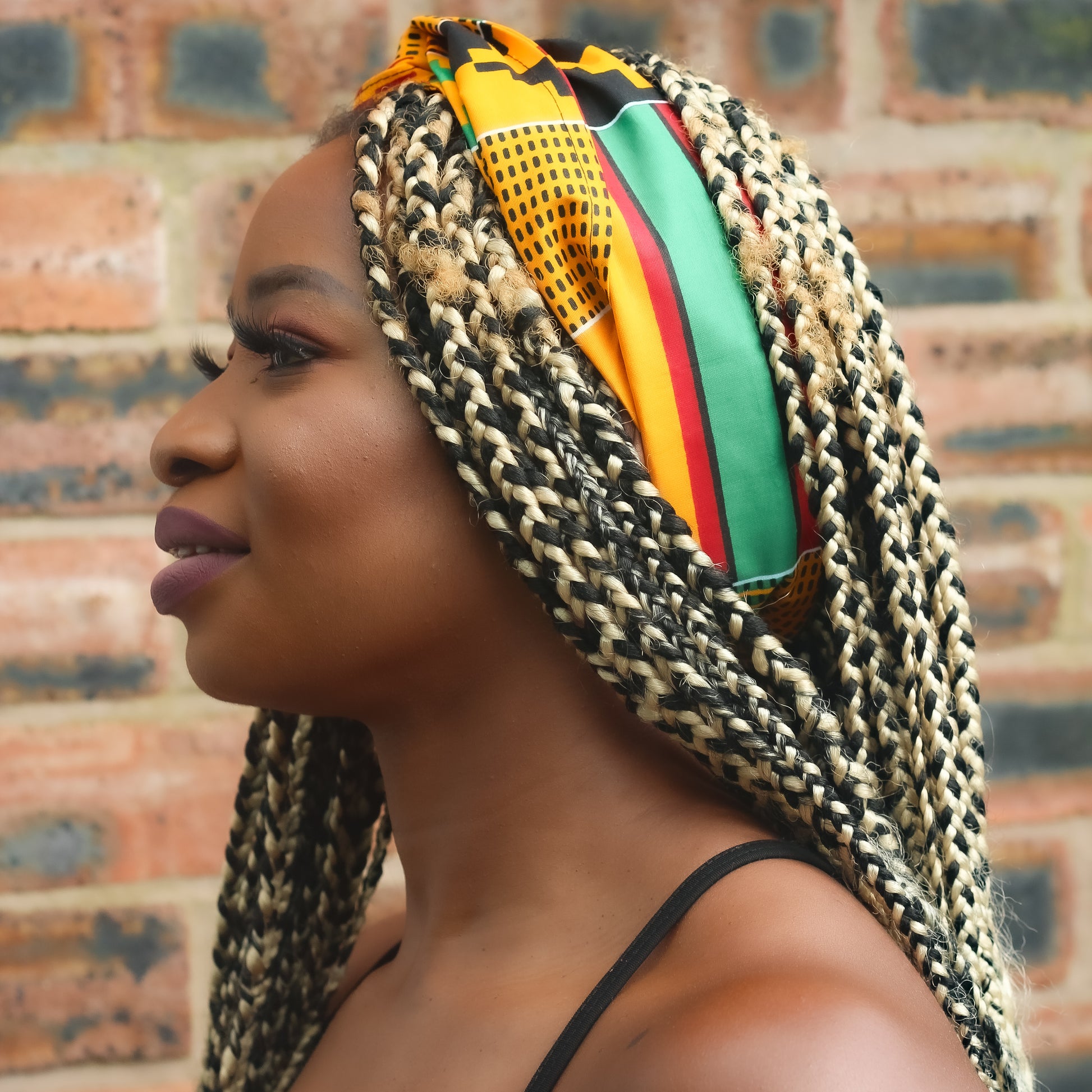 ellow, green, red, and black African print head wrap tied as headband in a geo-shaped pattern, made from sustainably sourced Ankara wax print.