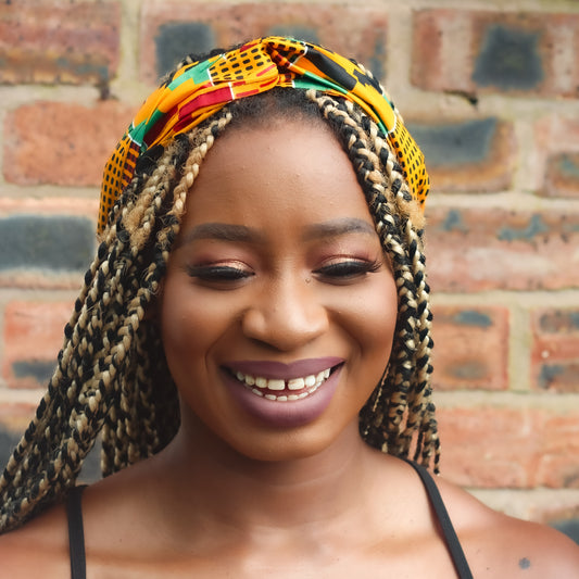 Yellow, green, red, and black African print head wrap tied as headband in a geo-shaped pattern, made from sustainably sourced Ankara wax print. 