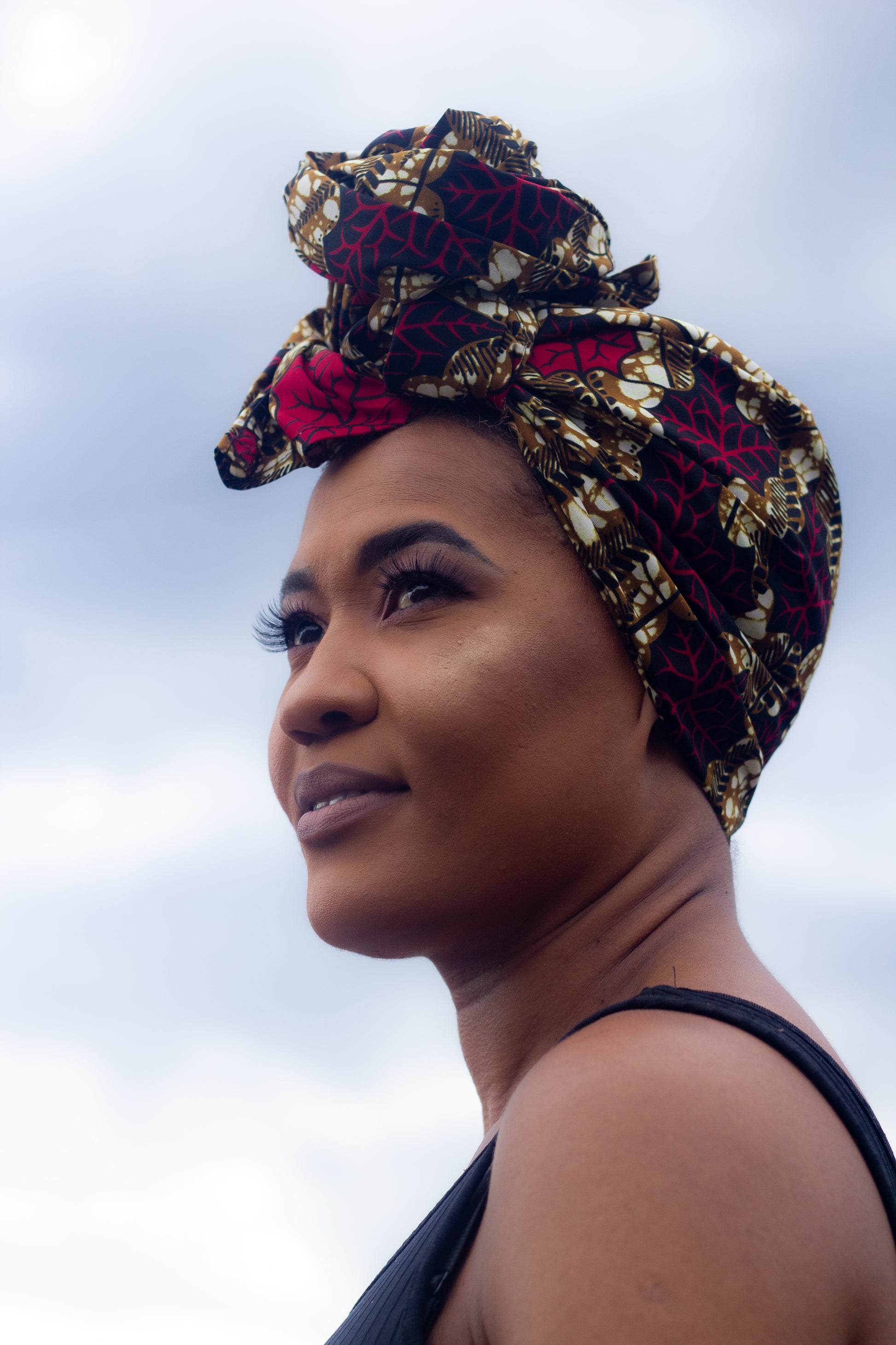 Brown, red, white, and black African print head wrap tied as a turban in a floral pattern, made from sustainably sourced Ankara wax print.