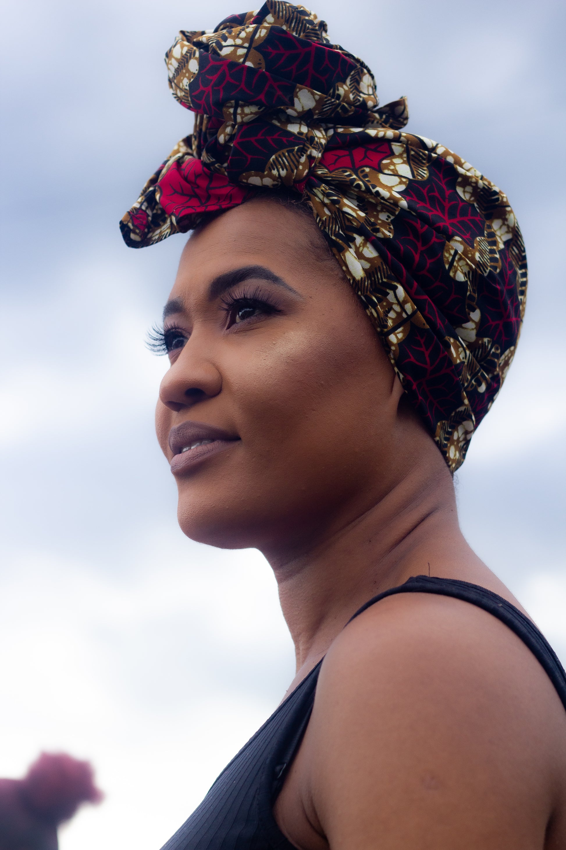 Brown, red, white, and black African print head wrap tied as a turban in a floral pattern, made from sustainably sourced Ankara wax print.