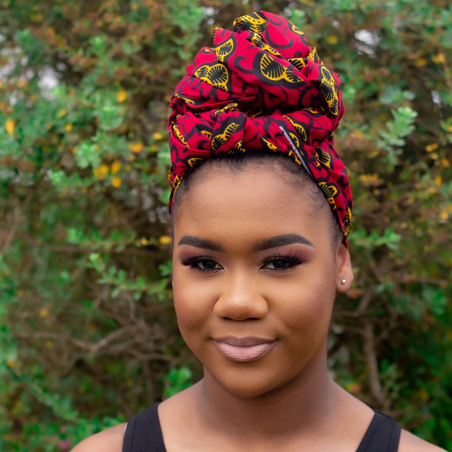 Red, yellow, and black African print head wrap tied as a turban in a floral pattern, made from sustainably sourced Ankara wax print. 