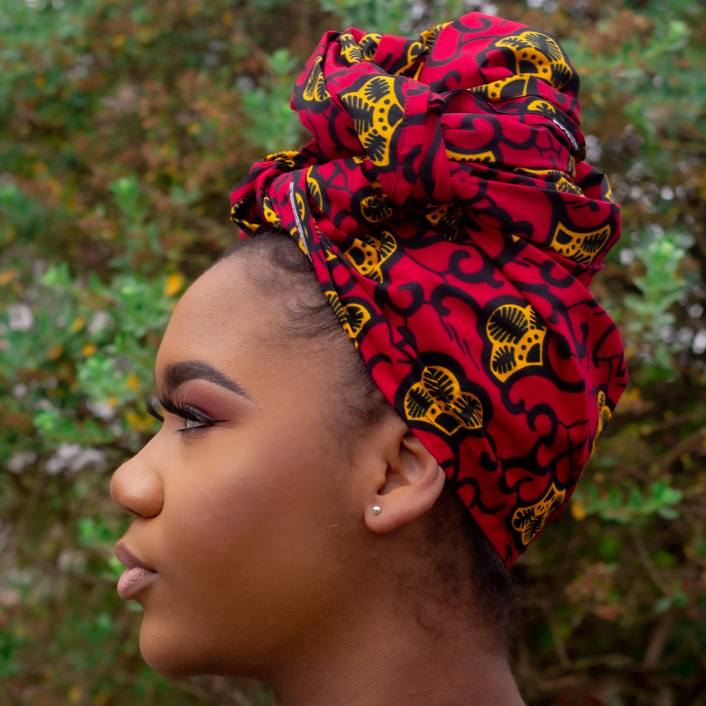 Red, yellow, and black African print head wrap tied as a turban in a floral pattern, made from sustainably sourced Ankara wax print. 