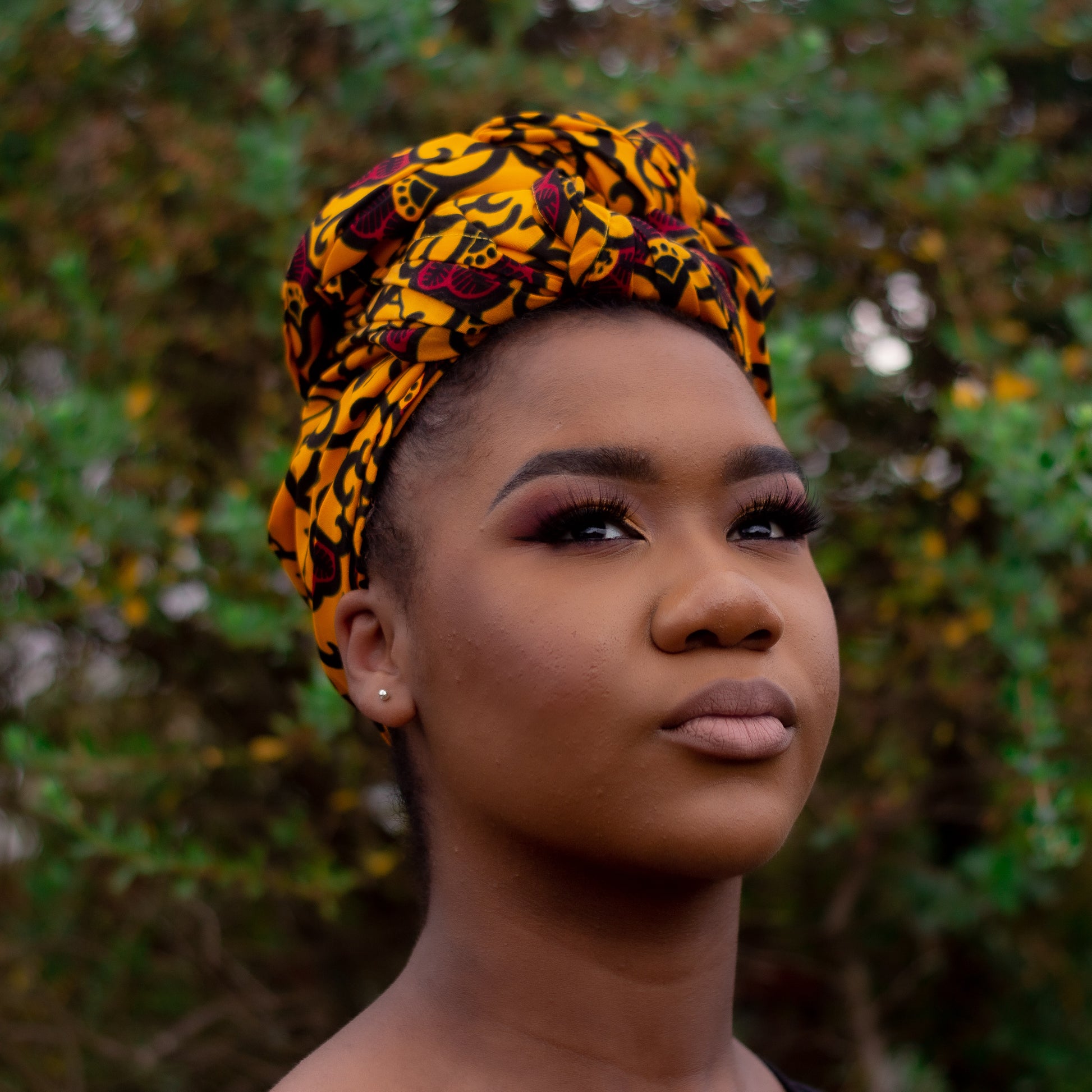 Yellow, red and black African print head wrap tied as turban in a floral pattern, made from sustainably sourced Ankara wax print.