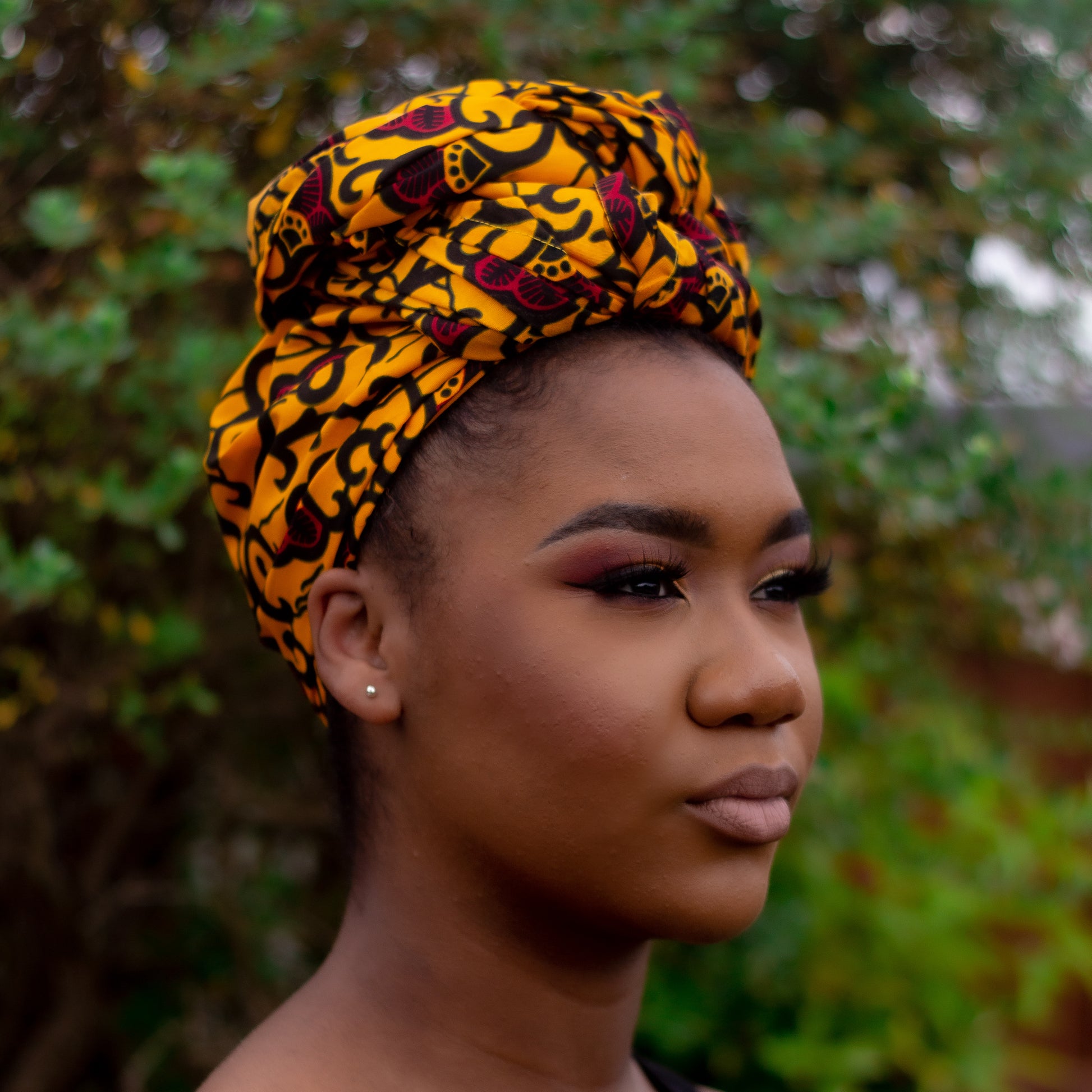 Yellow, red and black African print head wrap tied as turban in a floral pattern, made from sustainably sourced Ankara wax print.