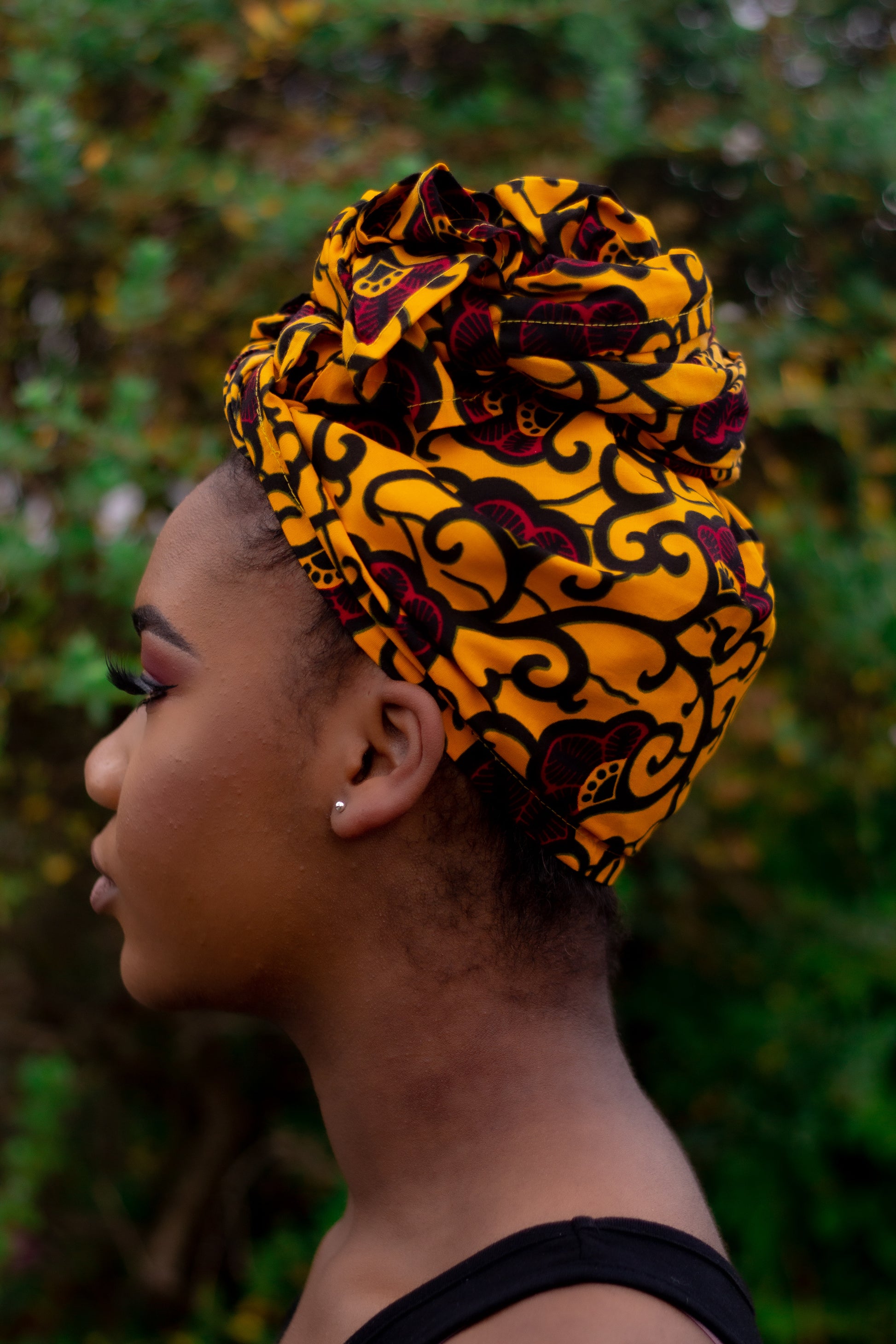 Yellow, red and black African print head wrap tied as turban in a floral pattern, made from sustainably sourced Ankara wax print.