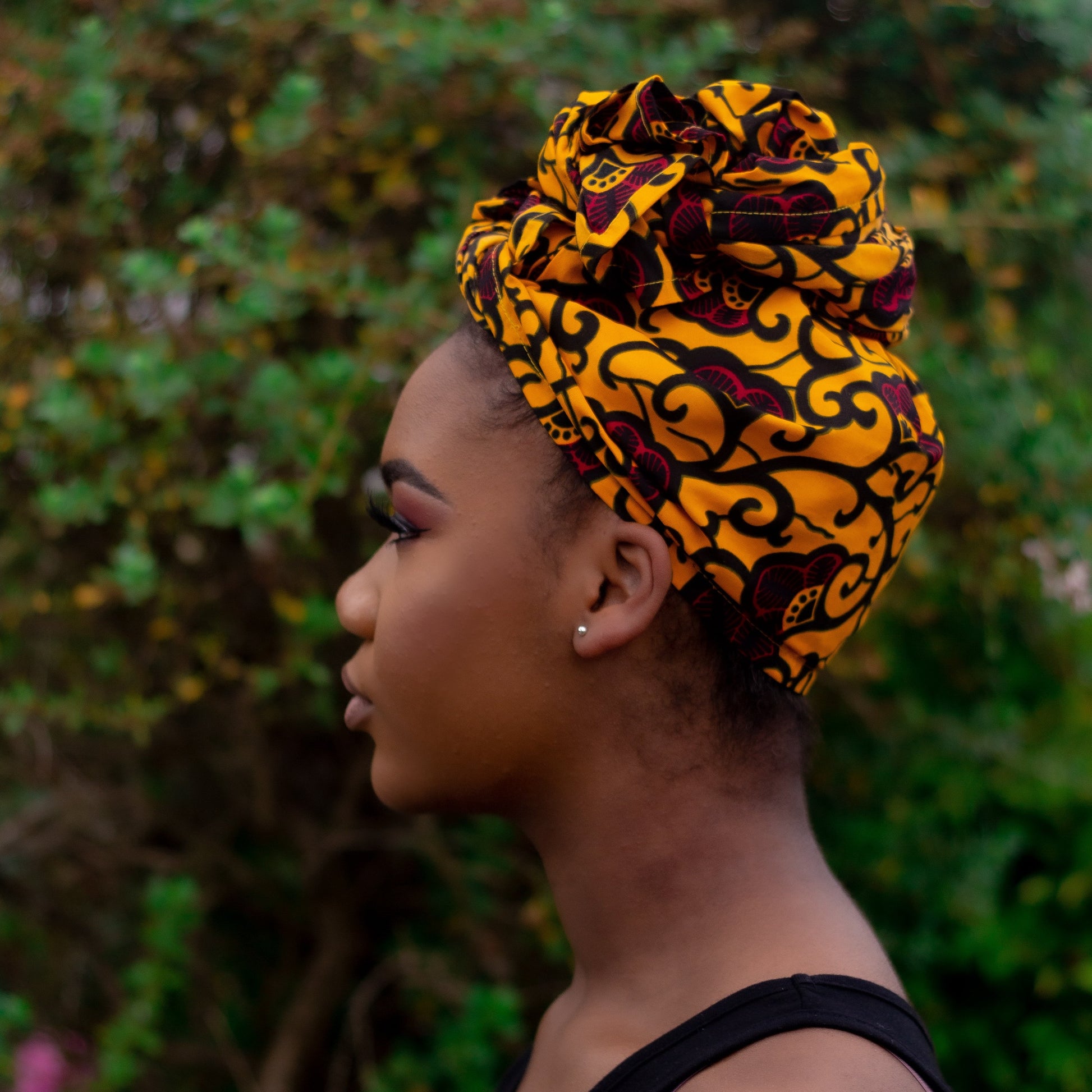 Yellow, red and black African print head wrap tied as turban in a floral pattern, made from sustainably sourced Ankara wax print. 