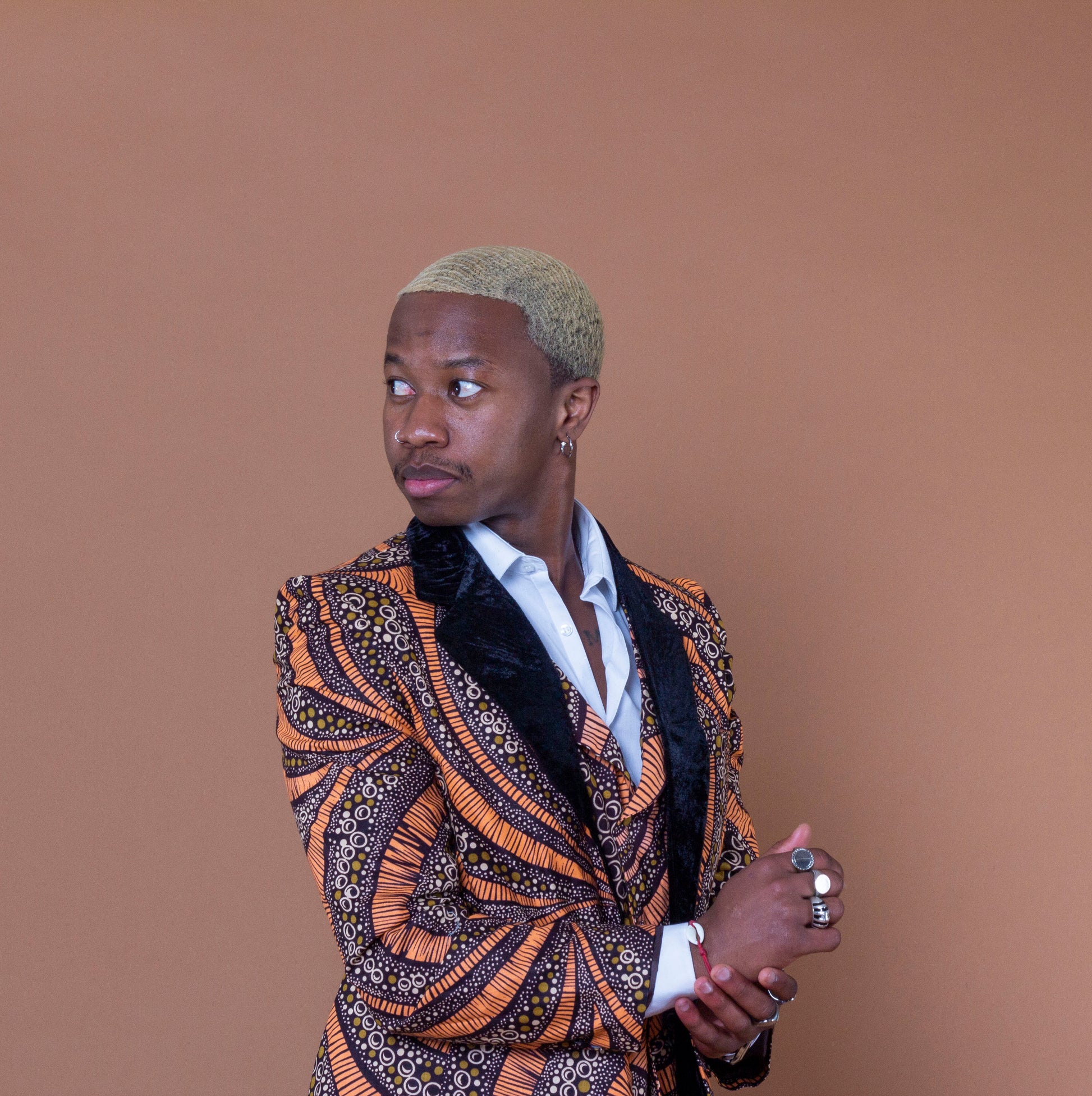 Men's blazer made from brown and orange african print ankara wax fabric finished with velvet lapels on the neckline worn with matching waistcoat and white collared shirt