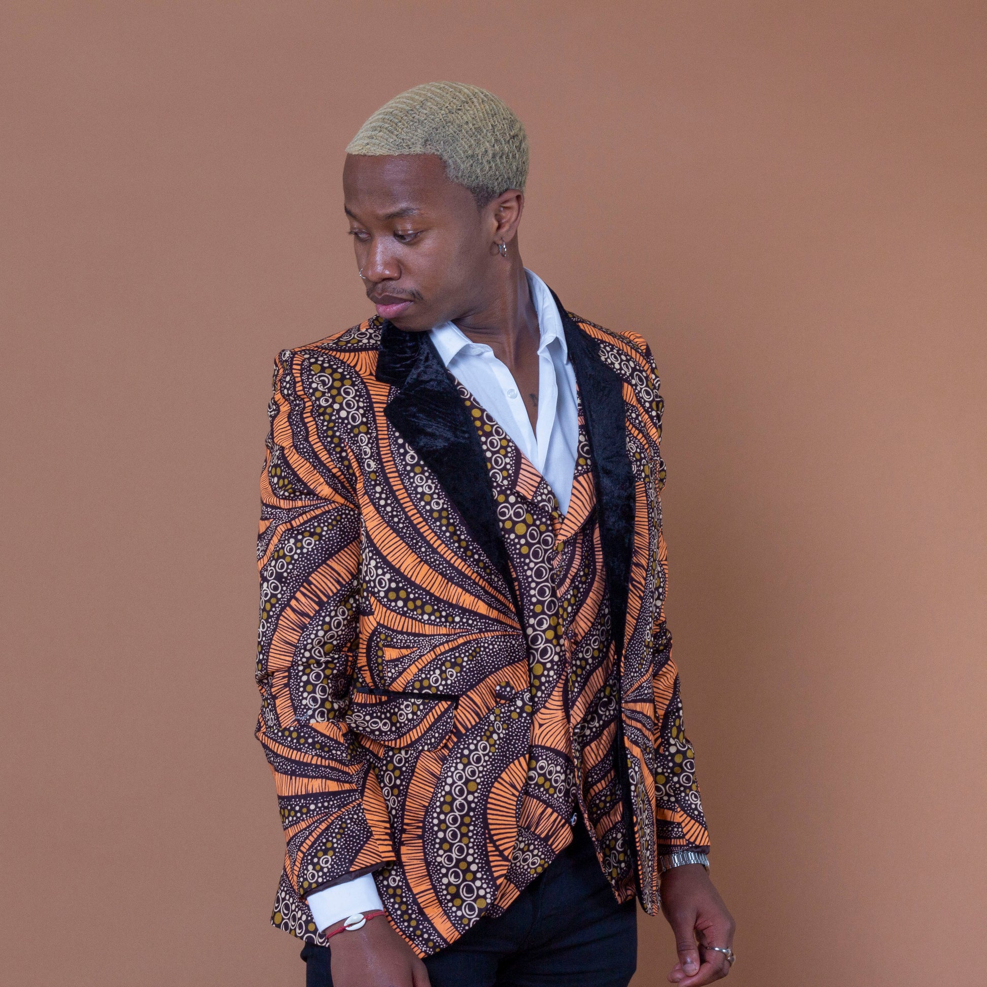 Men's blazer made from brown and orange african print ankara wax fabric finished with velvet lapels on the neckline and worn with matching waistcoat and white shirt