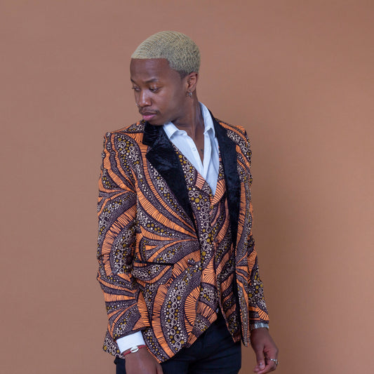 Men's blazer made from brown and orange african print ankara wax fabric finished with velvet lapels on the neckline and worn with matching waistcoat and white shirt