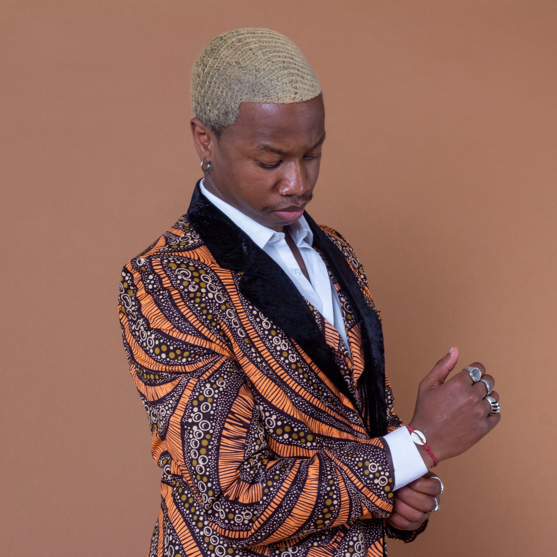 Men's blazer made from brown and orange african print ankara wax fabric finished with velvet lapels on the neckline and worn with matching waistcoat and white shirt