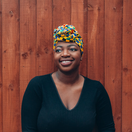 Yellow, green, blue, red and black African print head wrap tied as turban in a checkered  pattern, made from sustainably sourced Ankara wax print. 